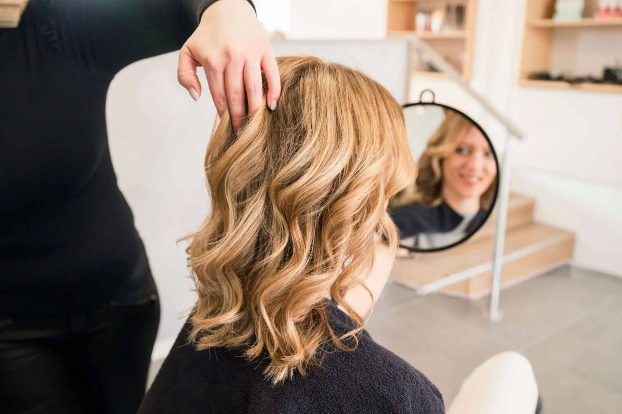 Friseurin zeigt einer Kundin im Spiegel die fertig gestylten, gewellten Haare