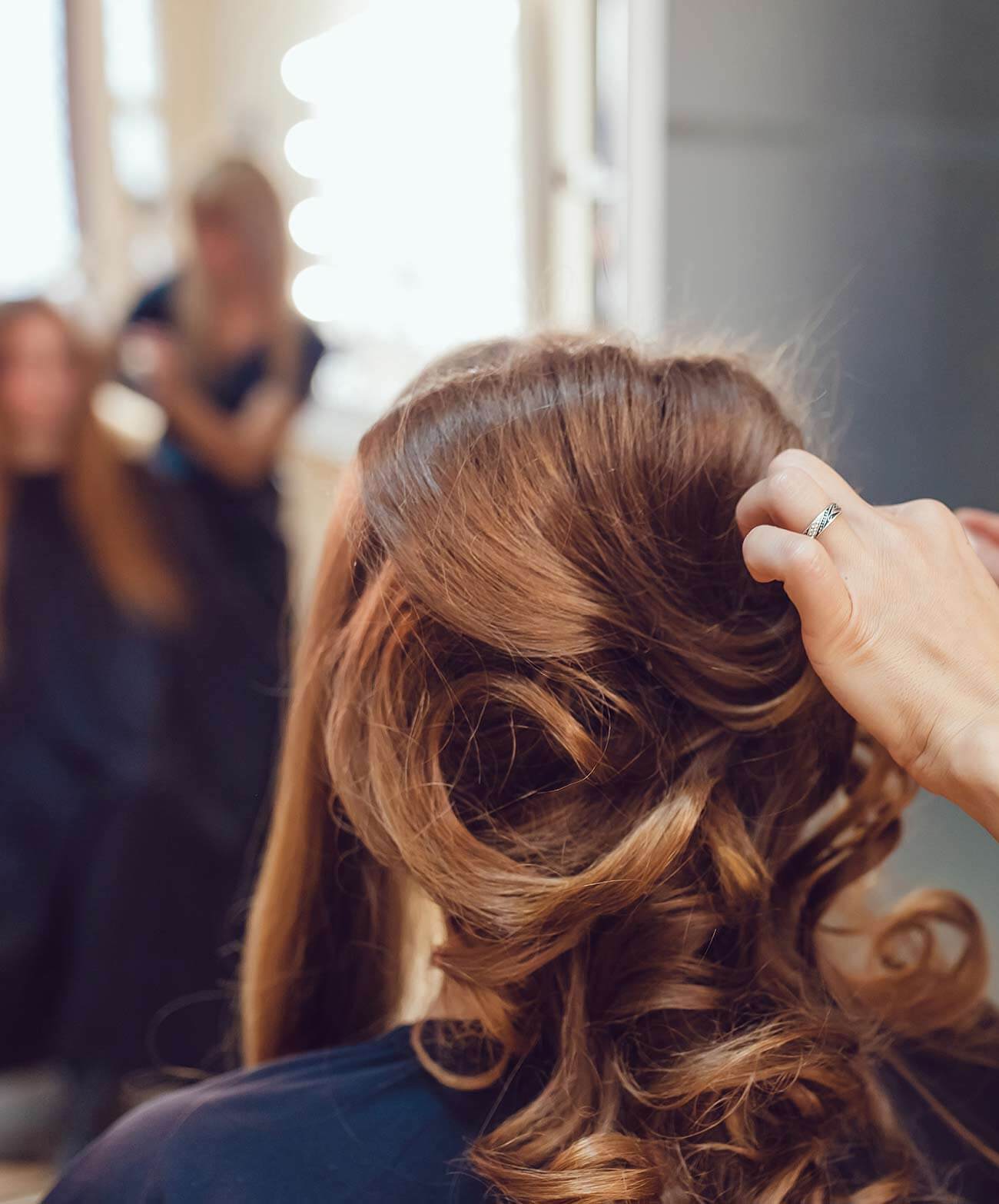 Friseurin steckt einer Kundin die gelockten Haare hoch